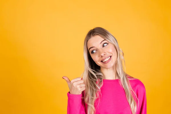 Sarı arka planda pembe bluzlu güzel Avrupalı kadın baş parmağıyla gülümsedi.