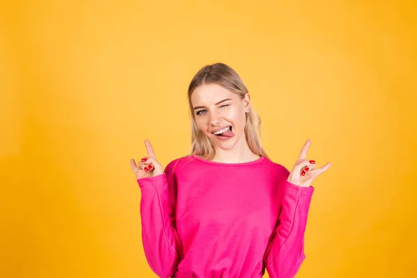 かなりヨーロッパの女性でピンクブラウスで黄色の背景ステッキング舌アウト行うロックシンボルとともに手アップ — ストック写真