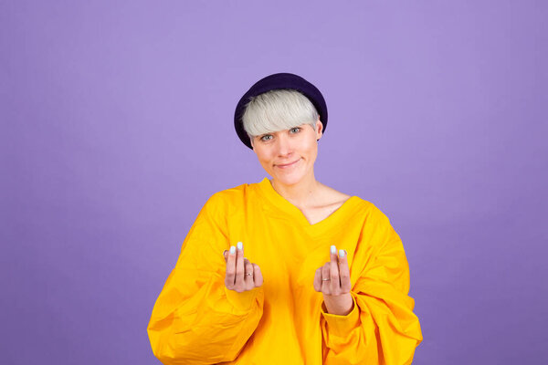 Stylish european woman on purple background standing rubbing fingers showing cash gesture asking for money