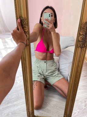 Bronz tenli, mükemmel vücutlu, kaslı, şortlu ve bikinili bir kadın. Sosyal medya, hikayeler, dikey dikey görüntüler için telefondaki aynadan fotoğrafımızı çek.