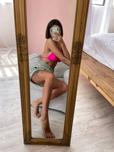 适合拥有完美身材 短裤和比基尼的晒黑的女人 在家里的镜子里为社交媒体 垂直拍摄自己的照片 — 图库照片