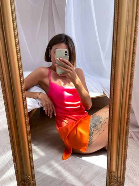 フィット日焼けした女性でかわいい明るい夏オレンジ色の絹のドレスに家で写真を撮る上の電話で鏡の中にソーシャルメディア — ストック写真