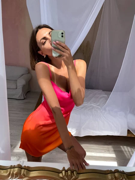 フィット日焼けした女性でかわいい明るい夏オレンジ色の絹のドレスに家で写真を撮る上の電話で鏡の中にソーシャルメディア — ストック写真