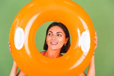 Yeşil arka planda pembe bikinili, parlak turuncu şişme yüzüklü, neşeli, neşeli, neşeli, neşeli, pozitif bir yaz kadını.