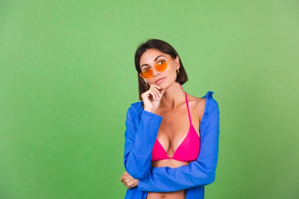夏天适合穿着粉色比基尼 蓝色衬衫 绿色背景的橙色太阳镜 快乐快乐而积极的女人 — 图库照片