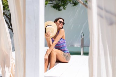 Güneşli yaz gününde, arka bahçedeki havuzda mayo giymiş güzel bir kadın. İnanılmaz sıcak havanın tadını çıkarıyor, güneş ışınlarını yakalıyor.