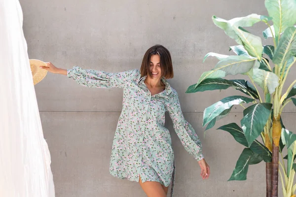 Yazlık elbise ve hasır şapka giymiş güzel bir kadın. Arka planda gri bir duvar. Neşeli, neşeli, mutlu, neşeli, neşeli, mutlu bir kadın.