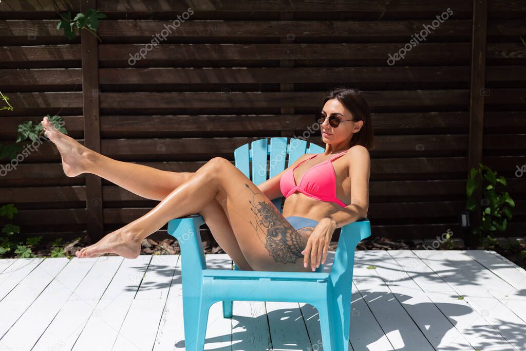 Beautiful tanned fit slender woman in bikini in backyard  posing on chair, summer vibes