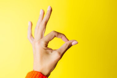 Kırmızı kazaklı kadının eli sarı arka planda iyi bir jest gösteriyor.