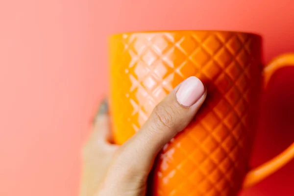 Woman's hand in red sweater holds orange  mug on red background