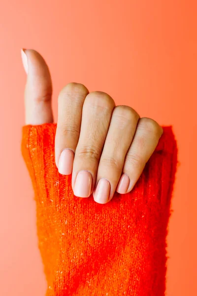 Woman\'s hand in red sweater shows gentle soft pink polish manicure on red background