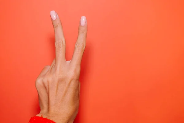 Woman\'s hand in red sweater shows V piece gesture on red background