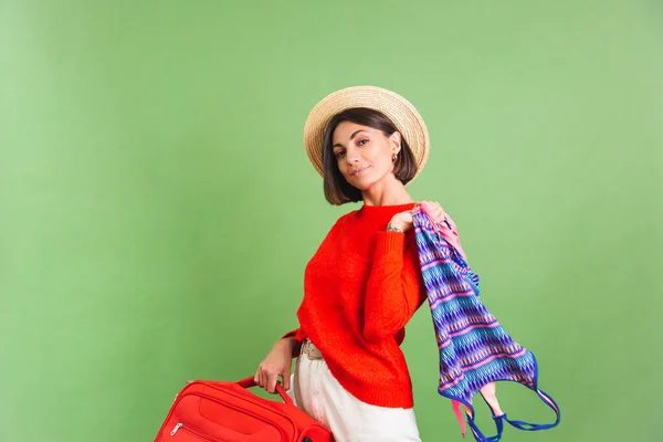 穿着绿色背景的红色休闲装 头戴草帽的女人拿着手提箱去度假 高兴地想着去哪里飞 — 图库照片