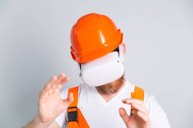 Bina koruyucu miğferinde yakışıklı bir mühendis ve gri arka planda kameralar havaya dokunuyor.