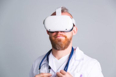 Sanal gerçeklik gözlükleriyle gri arka planda yakışıklı bir erkek doktor.