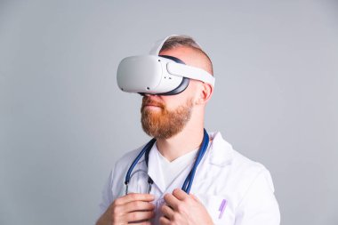 Sanal gerçeklik gözlükleriyle gri arka planda yakışıklı bir erkek doktor.