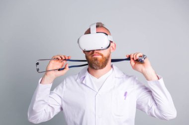 Sanal gerçeklik gözlükleriyle gri arka planda yakışıklı bir erkek doktor.