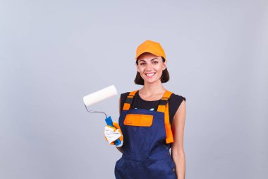 Gri arka planda paten fırçası olan, mutlu gülümseyen ressam kadın.