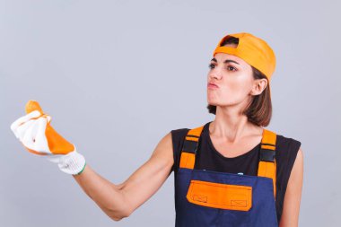 Tulumlu ve gri arka planda eldivenleri olan boyacı kadın hayal kırıklığına uğradığına yemin ediyor.