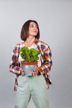Gri arka planda ekose gömlekli güzel kadın elinde bitki, bahçe konsepti mutlu bir gülümseme tutuyor.