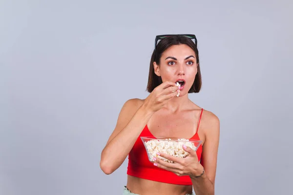 Beautiful woman on gray background in 3d cinema glasses looks aside focused on something having popcorn