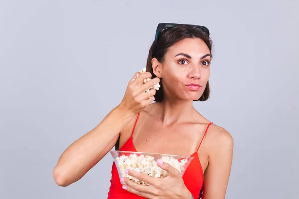 Beautiful woman on gray background in 3d cinema glasses looks aside focused on something having popcorn