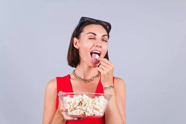 Beautiful woman on gray background in 3d cinema glasses with popcorn, cheerful happy emotions having delicious popcorn