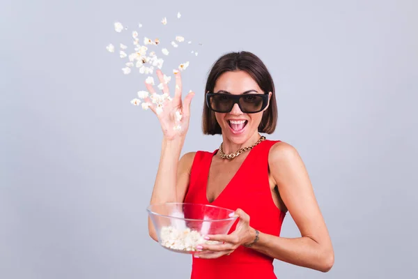 Beautiful woman on gray background in 3d cinema glasses with popcorn, cheerful excited throws popcorn to camera