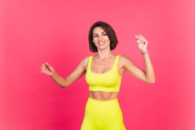 Pembe arka planda parlak spor kıyafetli güzel, fit bir kadın. Heyecanlı, hareketli, mükemmel vücut geliştirme motivasyonu.