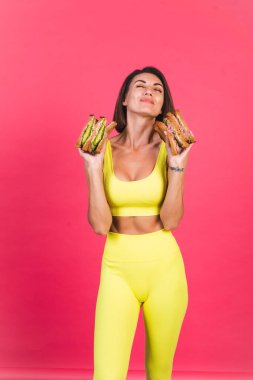 Pembe arka planda parlak spor kıyafetli güzel bir kadın. Sağlıklı avokado ve biftekli sandviç.