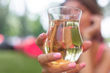Parlak pembe bluzlu güzel bir kadın boncuklu kolye takıyor yaz kafesinde çimenlere oturmuş taze limonata içiyor.