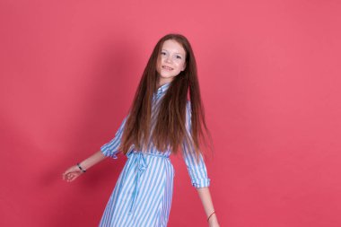 Mavi elbiseli 13 yaşındaki küçük kız pembe arka planda izole edilmiş neşeli hareketli mutlu gülümsüyor.