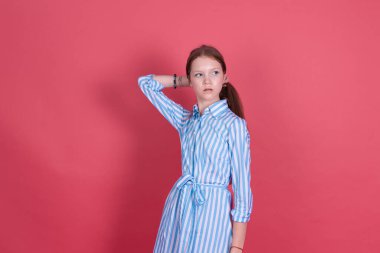 Mavi elbiseli 13 yaşındaki küçük kız. Pembe arka planda izole edilmiş. Ciddi bir saç teli var.