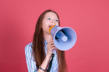 13 yaşında, mavi elbiseli, pembe arka planda izole edilmiş, megafonla bağıran mutlu, neşeli bir kız çocuğu.