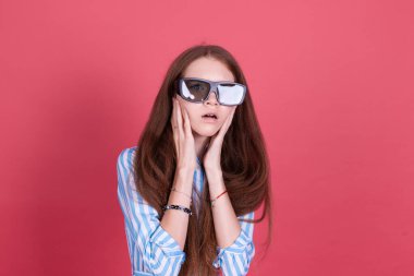 Mavi elbiseli 13 yaşındaki küçük bir kız çocuğu pembe arka planda izole edilmiş ve 3D sinema gözlüğü takıyor.