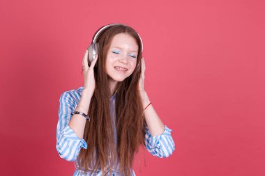 Mavi elbiseli 13 yaşındaki küçük bir kız çocuğu. Pembe arka planda kablosuz kulaklıklarla izole edilmiş parantezlerle mutlu bir şekilde gülümsüyor.