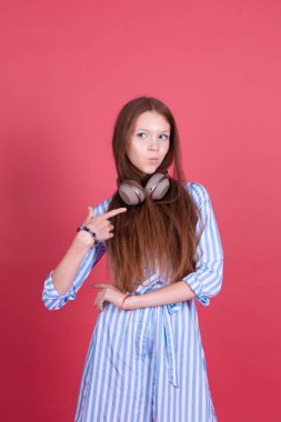 Mavi elbiseli 13 yaşındaki küçük bir kız çocuğu. Pembe arka planda kablosuz kulaklıklarla izole edilmiş parantezler var. 