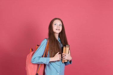 13 yaşında küçük bir kız çocuğu pembe arka planda izole edilmiş sırt çantalı ve kitaplı kız mutlu bir şekilde eğitim kavramını öğrenmeye bayılıyor.