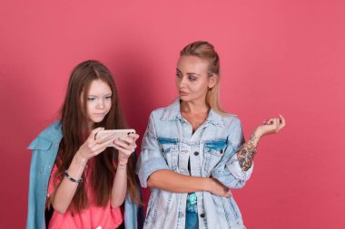 Terracotta arka planında kot ceketli modern anne ve kız, telefonda oyun oynayan kız ve annem sitem dolu bakışlarla bekliyor.