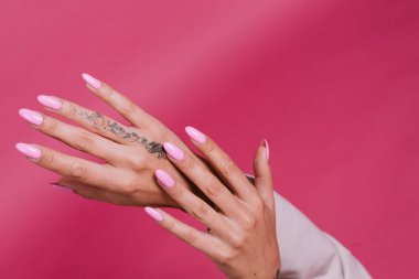 Zarif bej ceketli, altın mücevherli, pembe parlak jel tırnaklı, pembe arka planda poz veren zarif Avrupalı kadın.