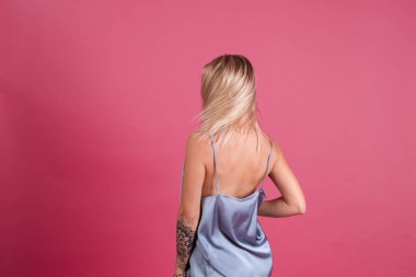 Zarif ipek elbiseli güzel sarışın kadın pembe arka planda soyutlanmış, makyajlı, iri dudaklı.