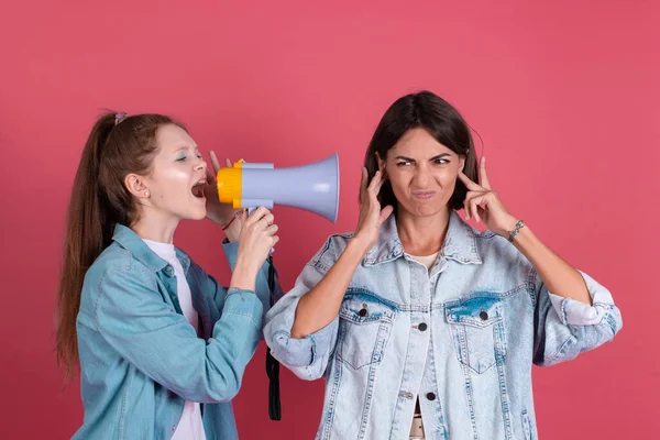 Modern mom and daughter in denim jackets on terracotta background girl shouting in megaphone mom stand by with ears cover with fingers