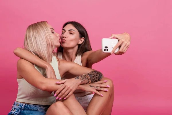 Dvě Dívky Přátelé Ležérní Růžovém Pozadí Fotit Selfie Mobilním Telefonu — Stock fotografie