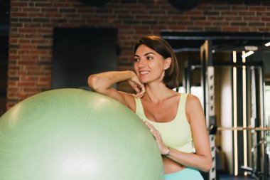 Fit caucasian beautiful woman in fitting sport wear at gym with fitball