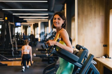 Fit caucasian beautiful woman in fitting sport wear at gym on abs core machine happy smiling