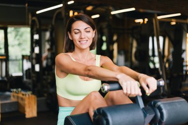 Fit caucasian beautiful woman in fitting sport wear at gym on abs core machine happy smiling