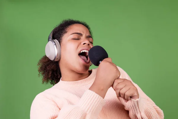 Yeşil Arka Planda Kablosuz Kulaklıkları Karaokede Şarkı Söyleyen Güzel Afrikalı — Stok fotoğraf