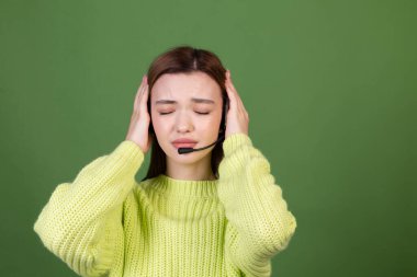 Mükemmel makyajlı, kahverengi dudaklı, iri dudaklı, yeşil arka planlı, kulaklıklı, çağrı merkezi çalışanı müdüründen bıkmış genç bir kadın.