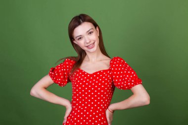 Mükemmel makyajlı genç bir kadın, kahverengi büyük dudaklı, puantiyeli kırmızı elbiseli, yeşil arka planda sevimli, gülümseyen pozitif yüzlü.