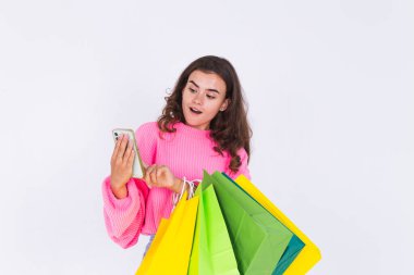 Çilli, hafif makyajlı, beyaz arka planda, alışveriş çantalı ve cep telefonlu genç bir kadın şaşkınlık içinde.